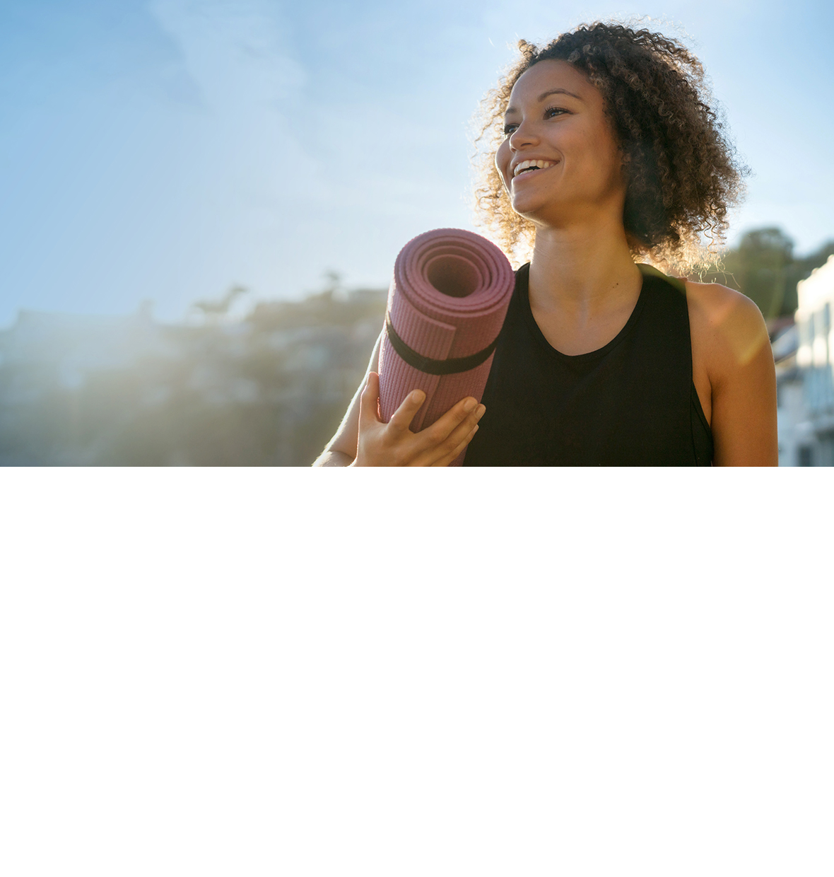 Lady with yoga mat in the sunny outdoors smiling to her right