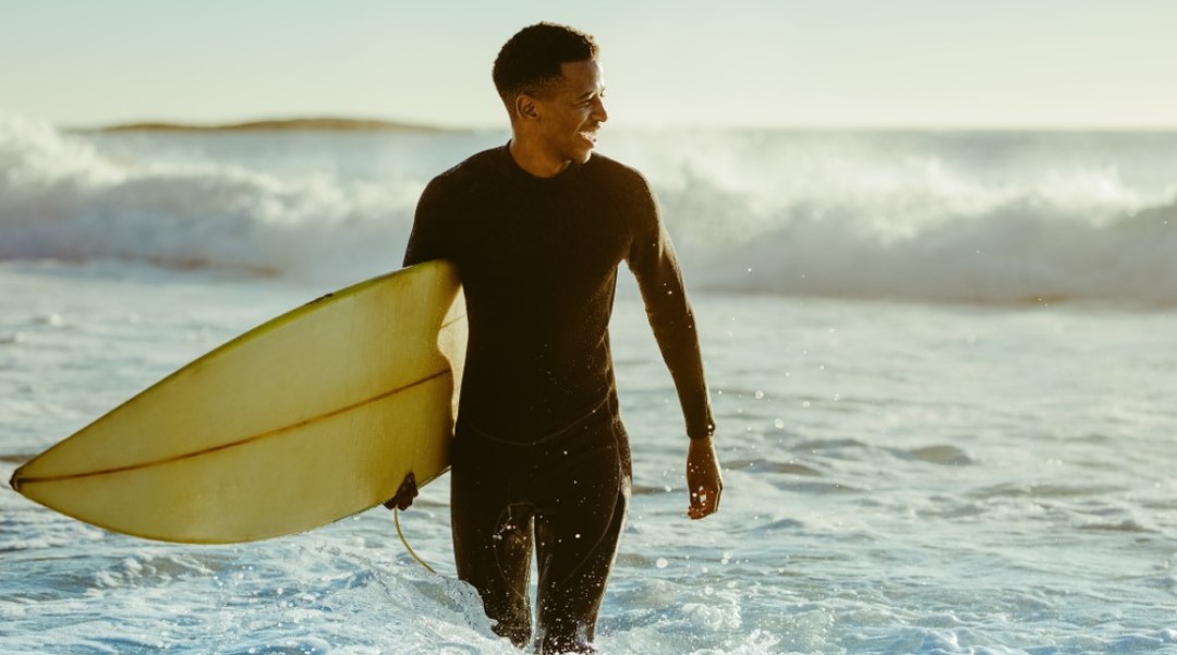 Man looking to his left on the beach carrying a surfboard